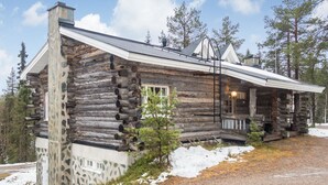 A rustic log cabin with a stone foundation, a chimney, and a porch with a lamp.
