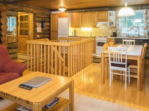 Interior acogedor de una cabaña con una mesa de comedor de madera, sillas, una zona de cocina con armarios de madera y una chimenea.