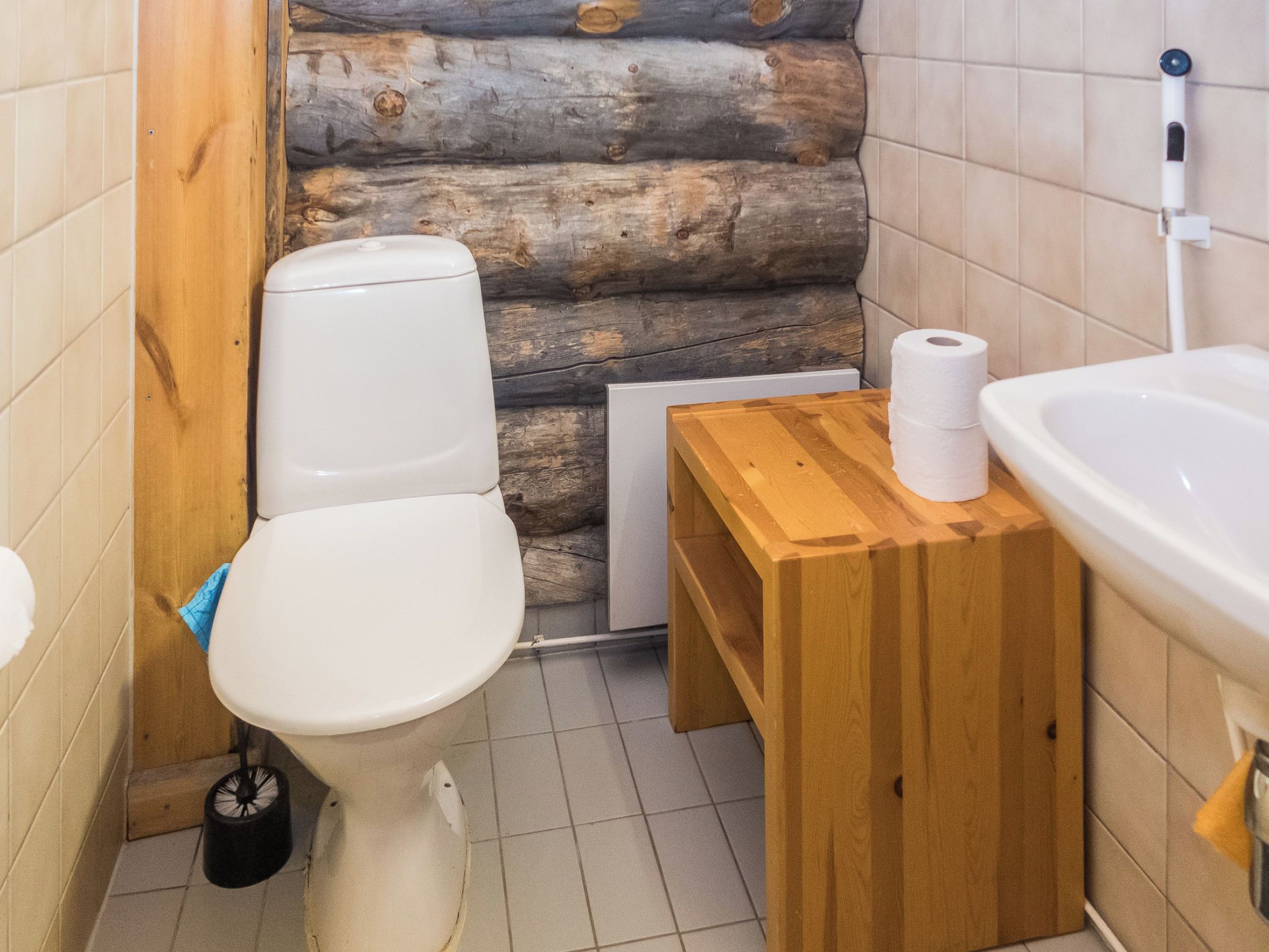 Une petite salle de bain comprenant des toilettes, une table d’appoint en bois avec un rouleau de papier toilette et un lavabo blanc.