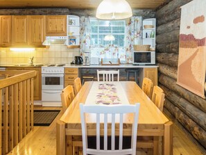 A wooden cabin kitchen with a dining table, chairs, a stove, a microwave, and a window with curtains.