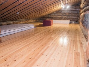 Habitación estilo ático en una cabaña de madera, con piso de madera, un taburete otomano rojo y un colchón.