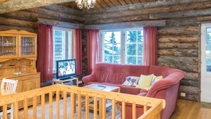 A cozy log cabin interior with a wooden dining table, a red sofa, a television, and a wooden cabinet.