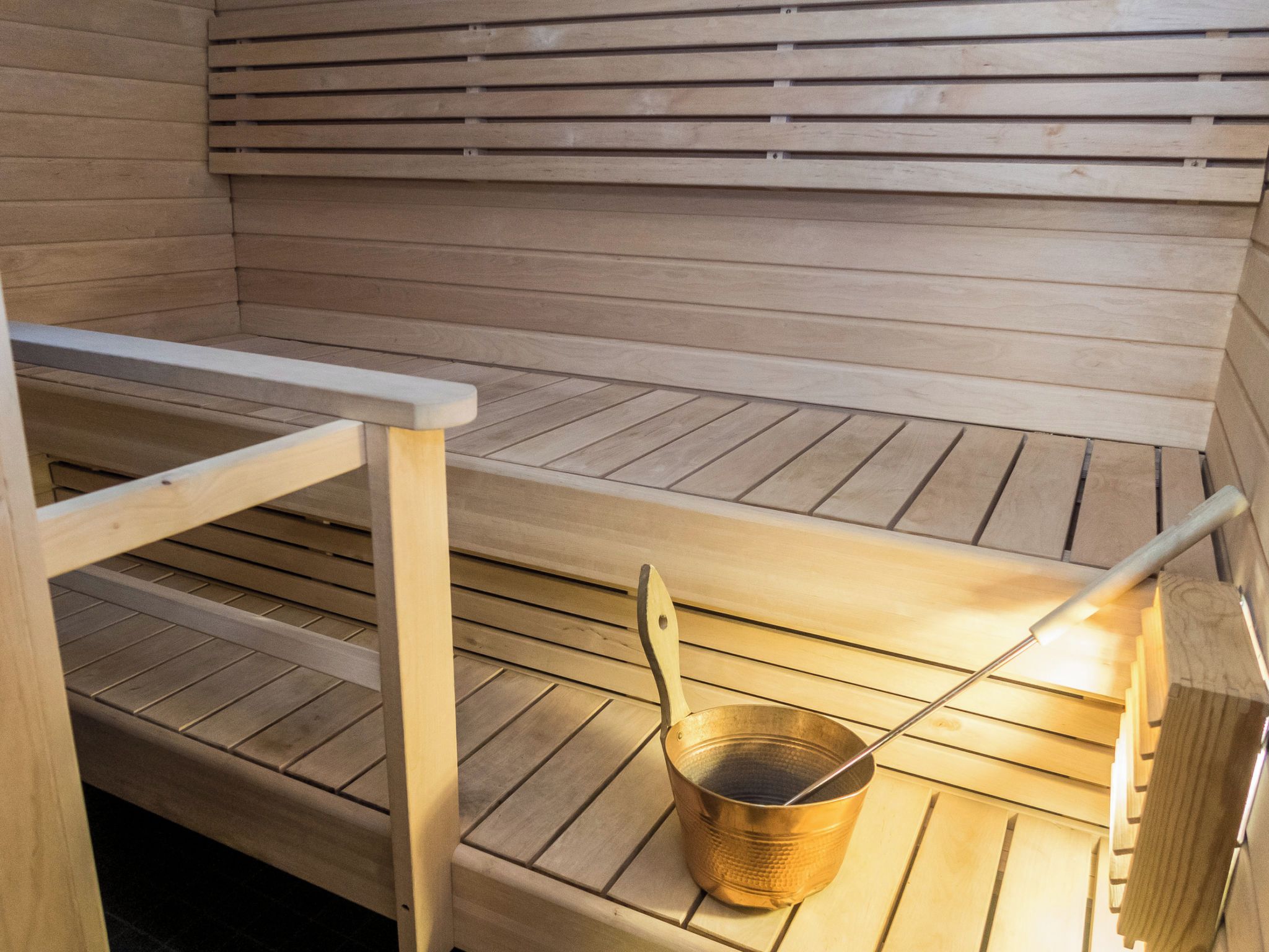 A sauna with wooden benches and a metal bucket.