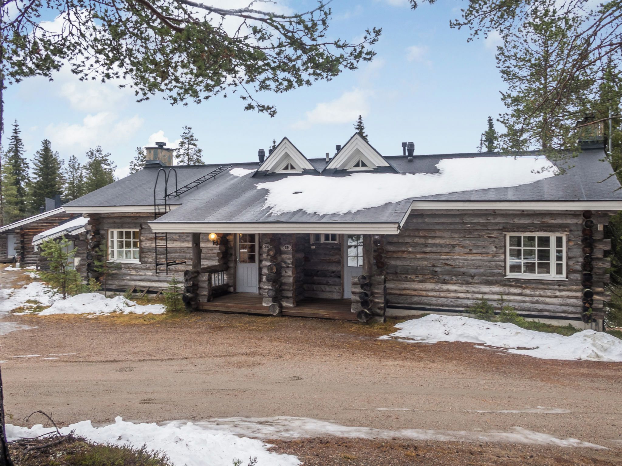 Une cabane en rondins avec un porche et une cheminée, entourée de neige.