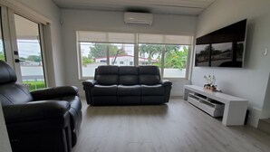 Uma sala de estar com um sofá de couro preto, um rack branco e uma janela grande com vista para casas e árvores.