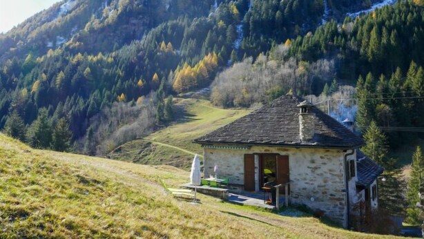 A stone house with a sloped roof, a small porch, and a view of a forested mountain. - Rustico Stübii by Interhome (Campo Blenio)
