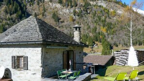 A stone building with a tiled roof, outdoor seating with green chairs, and a mountainous backdrop. - Rustico Stübii by Interhome (Campo Blenio)