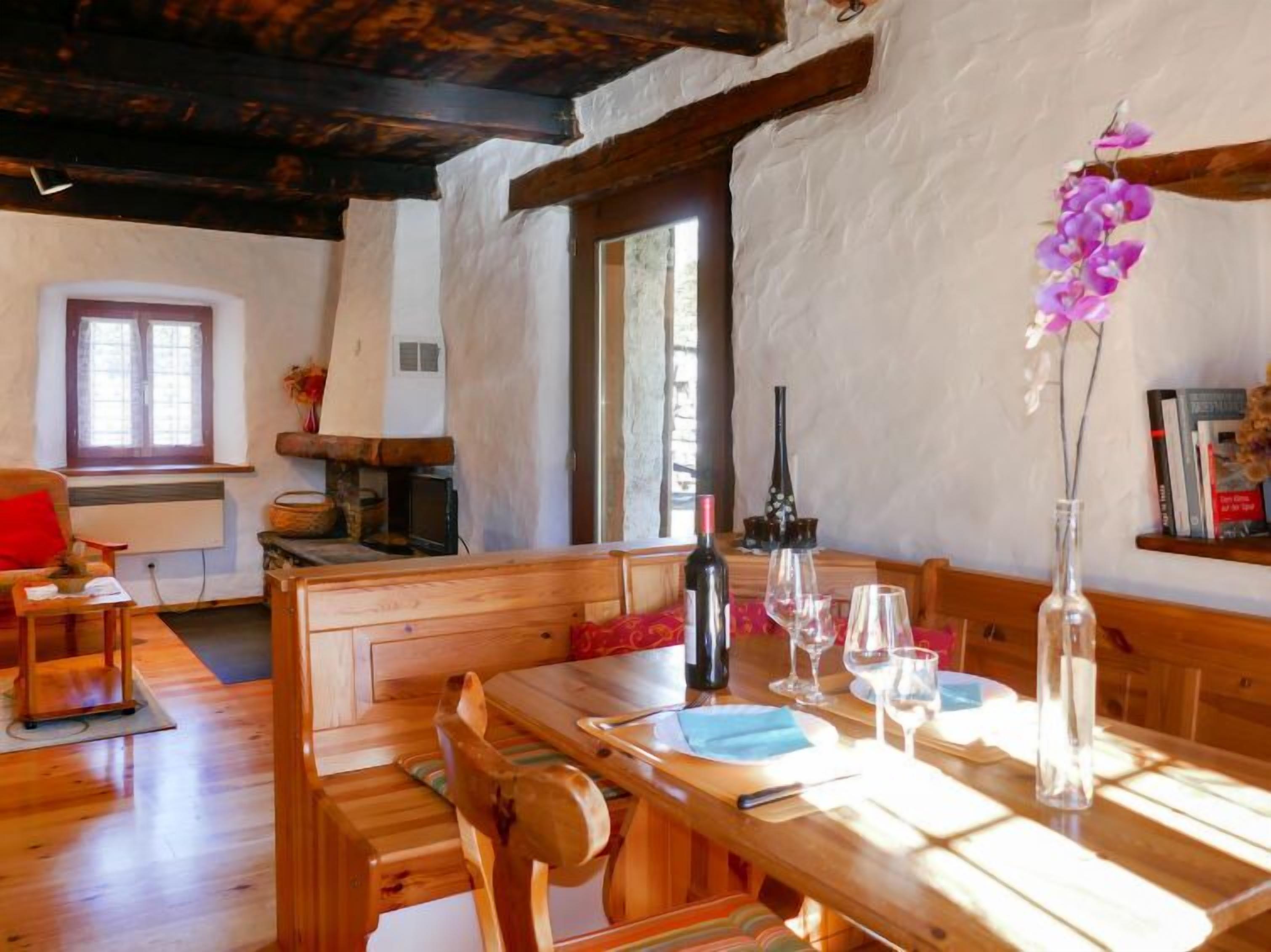 A wooden dining table set with plates, glasses, and a wine bottle, with a bench and chairs around it.