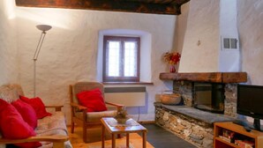 A cozy living room with a stone fireplace, a wooden sofa with red cushions, a small table, and a television on a wooden stand. - Rustico Stübii by Interhome (Campo Blenio)