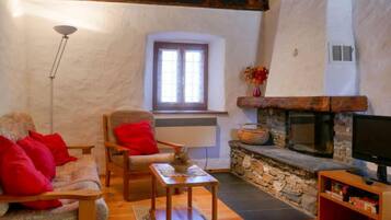 A cozy living room with a stone fireplace, a wooden sofa with red cushions, a small table, and a television on a wooden stand.