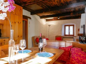 Un coin repas avec des meubles en bois, une table dressée pour deux personnes et une fenêtre avec des rideaux.