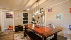 A dining area with a wooden table, benches, and chairs. There is a rug on the floor, a clock on the wall, and artwork on the walls. - Crabbin Cabin - Spacious, Seasonal Riverside Home (Midway)