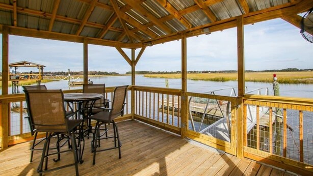 A covered outdoor deck with a wooden table and chairs, overlooking a body of water and a dock. - Crabbin Cabin - Spacious, Seasonal Riverside Home (Midway)