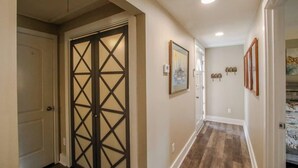 A hallway with a wooden floor, a door with a black cross pattern, and framed pictures on the wall. - Crabbin Cabin - Spacious, Seasonal Riverside Home (Midway)