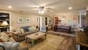 A spacious living room with a ceiling fan, a dining area with a wooden table and chairs, and a kitchen area visible through an open doorway. - Crabbin Cabin - Spacious, Seasonal Riverside Home (Midway)