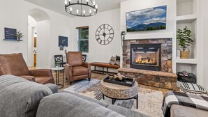 A living room with a stone fireplace, leather chairs, a large clock, and a mounted TV.