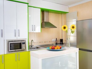 A modern kitchen with white cabinets, a stainless steel refrigerator, a built-in oven, and a sink.