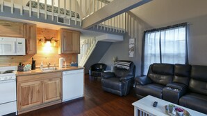 A spacious living area with a kitchen, a black leather sofa, and a staircase leading to an upper level. - Memory Maker Condo - Great Location - Updated - Walk to Restaurant and Store! (Branson)