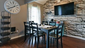 A dining area with a stone wall, a mounted clock, and a television. - Memory Maker Condo - Great Location - Updated - Walk to Restaurant and Store! (Branson)