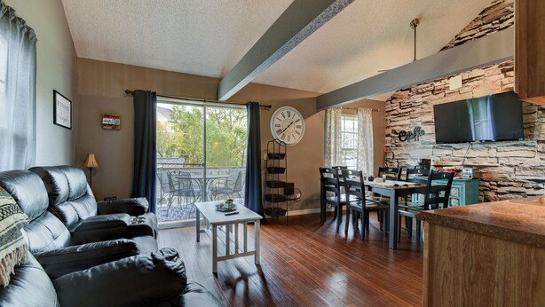 A living room with a stone wall, a dining area, and a kitchen with a TV. - Memory Maker Condo - Great Location - Updated - Walk to Restaurant and Store! (Branson)