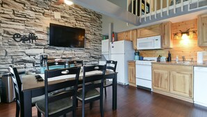 A modern kitchen with stone walls, wooden cabinets, a dining area with a table and chairs, and a flat-screen TV mounted on the wall. - Memory Maker Condo - Great Location - Updated - Walk to Restaurant and Store! (Branson)