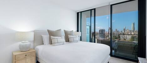 Ein modernes Schlafzimmer mit einem großen Bett, einem Nachttisch und Blick auf die Stadt durch raumhohe Glasfenster.