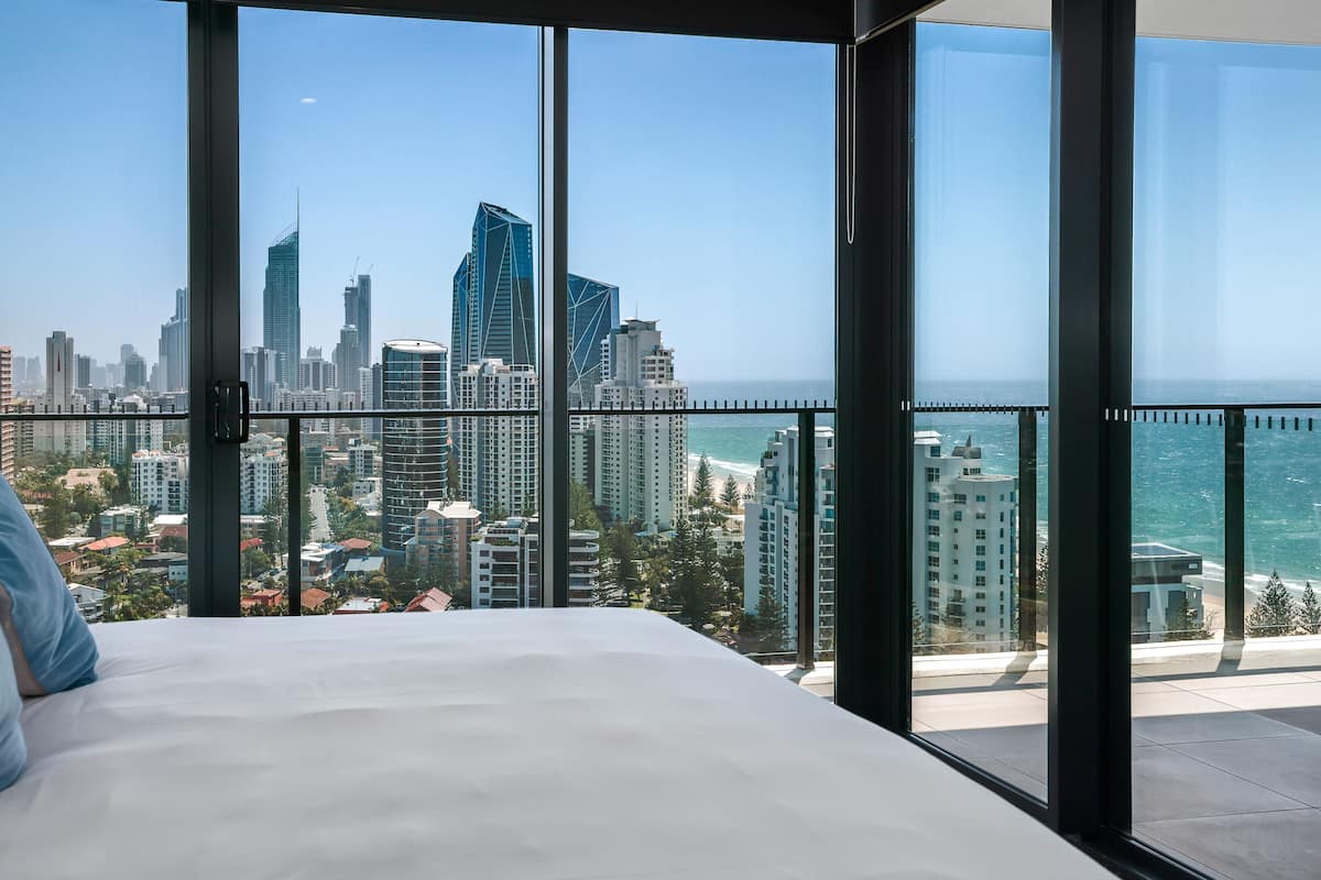 A bedroom with a large window overlooking a city skyline and the ocean.