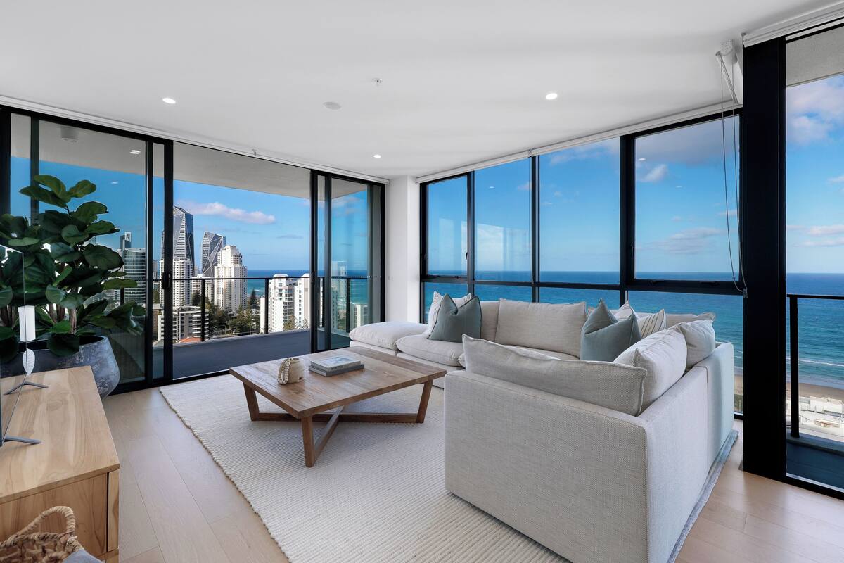 A modern living room with a large window overlooking a cityscape and the ocean.