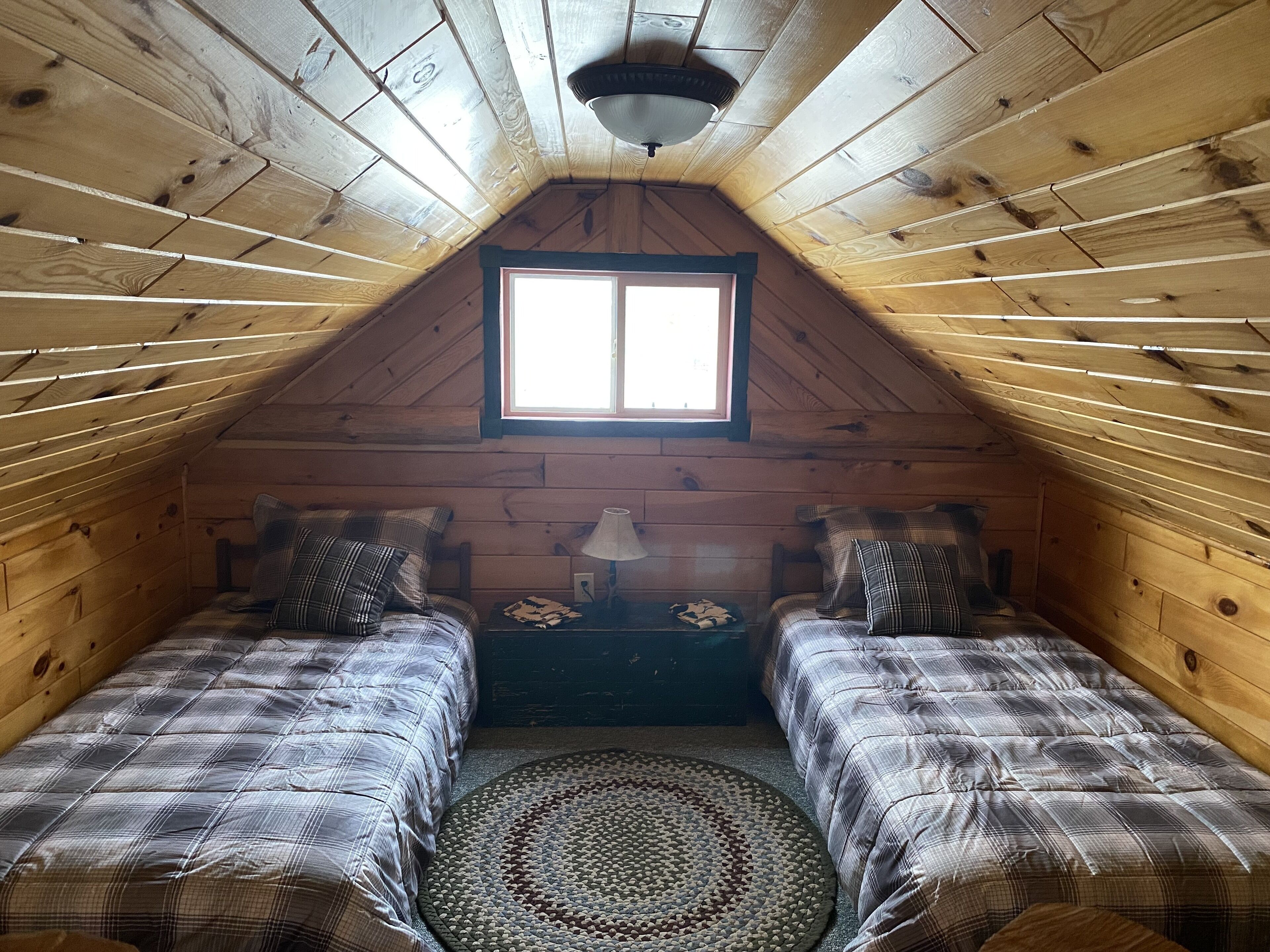 Une chambre mansardée chaleureuse, avec deux lits, une fenêtre et un ventilateur de plafond.