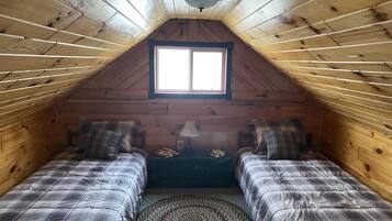 A cozy attic bedroom with two beds, a window, and a ceiling fan.