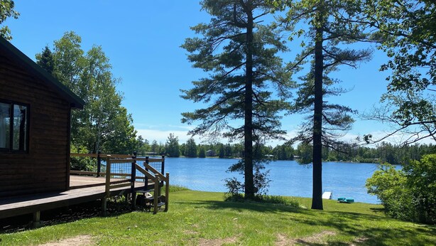 Una cabaña con terraza que da a un lago, rodeada de árboles.