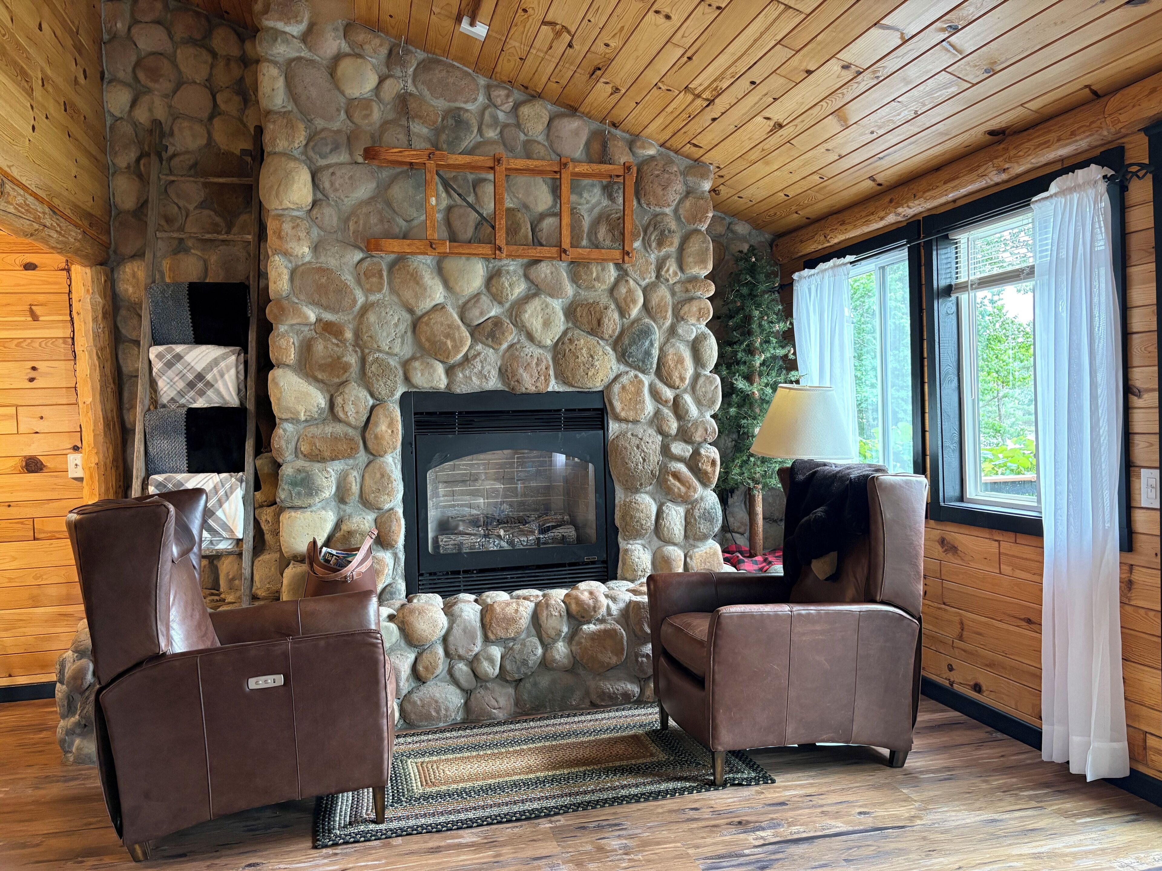 A stone fireplace with a black glass front, wooden ceiling, and two leather armchairs.