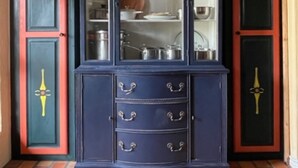 Een donkerblauwe kast met glazen deuren, rode accenten en decoratieve versieringen.