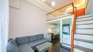A modern living room with a grey sofa, a glass coffee table, and a wooden staircase. - Le Lu (Jiaoxi)