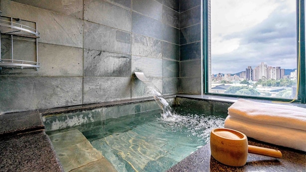 A stone-tiled bathroom with a view of a cityscape through a large window. - Le Lu (Jiaoxi)