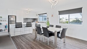 Une cuisine moderne avec des meubles blancs, un réfrigérateur en acier inoxydable et un coin repas comprenant une table blanche et des chaises noires.