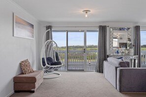 A modern living room with a hanging chair, a sofa, a small ottoman, and a large mirror. - Ocean Pearl by Ready Set Stay - 10 min Walk to the Beach, BBQ (Surf Beach)