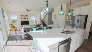 Una cocina moderna con armarios blancos, una isla grande, electrodomésticos de acero inoxidable e iluminación colgante color aguamarina.