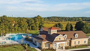 Una casa grande con piscina, cancha de tenis y vista a un área boscosa.