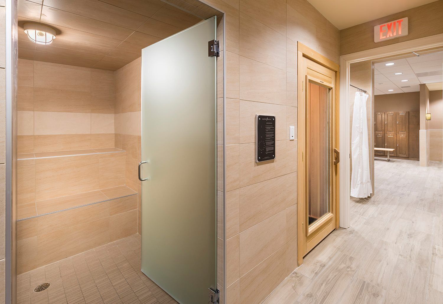 Un pasillo con una puerta de vidrio satinado, una puerta de madera con letrero de salida y un cartel en la pared con texto.