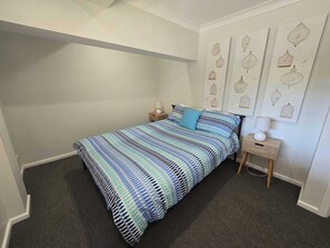 A bedroom with a bed, a nightstand, a lamp, and wall art. - Fairwater In Mollymook (Mollymook)