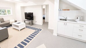 Un espacio habitable moderno con sofá, mesa de centro, televisor y una zona de cocina con lavaplatos y armarios.