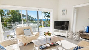 Una sala de estar moderna con un televisor grande, asientos cómodos y vistas al exterior.
