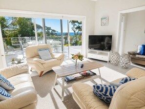 A modern living room with a large TV, comfortable seating, and a view of the outdoors.