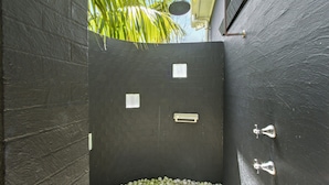 A small, enclosed shower area with a black tiled wall, a showerhead, and a small window. - Sticks By The Sea at Manyana (Manyana)