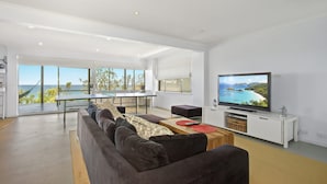 A modern living room with a large TV, a sofa, a dining table, and a view of the sea. - Sticks By The Sea at Manyana (Manyana)