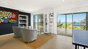 A modern living room with a large window, a bookshelf, a sofa, and a table. - Sticks By The Sea at Manyana (Manyana)