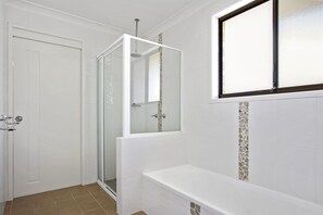 A bathroom with a glass shower enclosure, a white bathtub, and a door.