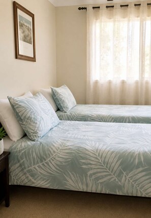 A bedroom with two beds, a framed picture on the wall, and a window with sheer curtains. - Seascape Carroll Avenue (Mollymook)