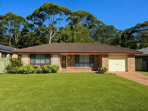 A single-story house with a tiled roof, a garage, and a well-maintained lawn. - Seascape Macleay Street (Narrawallee)